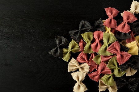 farfalle Raw farfallini colored italian pasta on a wood black textured background. Close-up view...