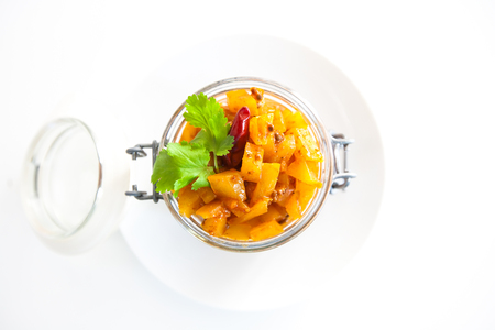 Homemade mango chutney in a glass jar with spices and mangoes isolated on a white backgroundの写真素材