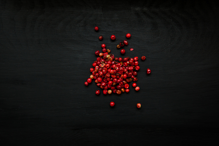 Close-up image of pepper rose, pink peppercorns on black wood background, view above