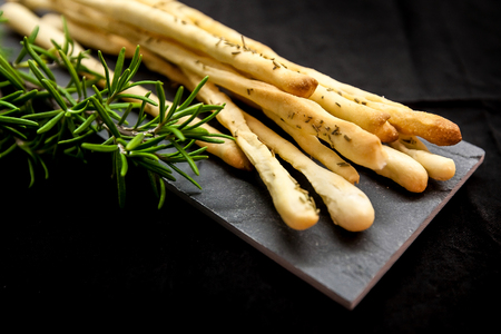 Italian grissini or salted breadsticks with fresh rosemary on a dark brown stone backgroundの写真素材