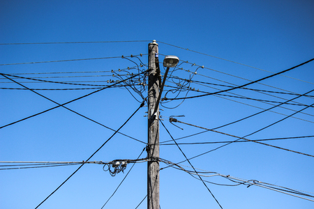 high voltage electricity pole with chaotic wiring, street lamp and blue skyの写真素材