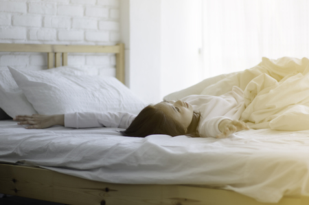 women sit at the edge of the bed. And stretching his arms to relax in the morning.Wake up in the morning.Stretching after waking.Warm tone.Do not focus on the object.の写真素材
