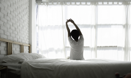 Men sit at the edge of the bed. And stretching his arms to relax in the morning.Wake up in the morning.Stretching after waking.の写真素材
