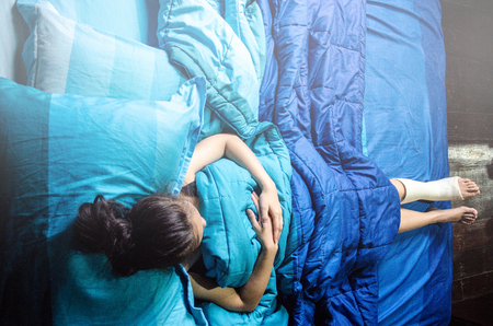 Asian girl is sleeping on blue bed in bedroom.Ankle strap for treating torn wound of foot injury. On the blue floor.Foot and ankle strap protects against injury.Do not focus on objects.の写真素材