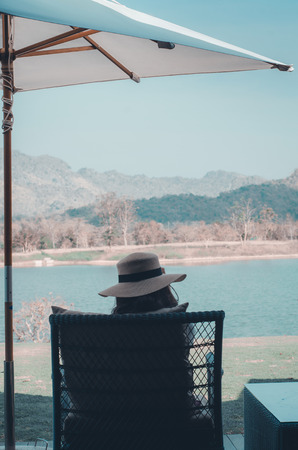 Woman wearing a white hat Sitting at a chair.White umbrella.Asian women sitting by the river.の写真素材