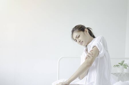 Asian women wearing white pajamas In the bedroom She has a lot of pain on her arm.