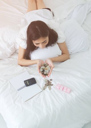 Asian women put the silver coins in the heart, including calculators and notebooks. On the mattress to save income. Concept saving.Do not focus on the main object of this image.の写真素材