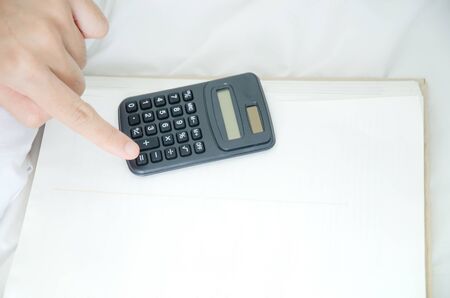 Black thinking calculator placed on the books and fingers of women pointing at the calculator keys.Copy space.の写真素材