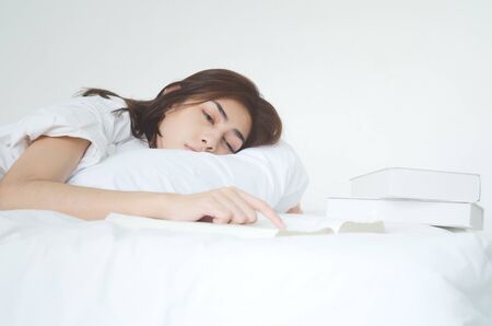 Women are reading books And she is having sleepiness And slept beside her book On the bed in the room.o not focus on the main object of this image.Copy space.の写真素材