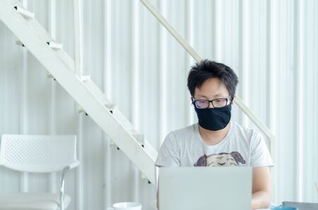 Asian Men Wearing Glasses Wearing a black mask Is working.A sick man sitting at work.In the white...
