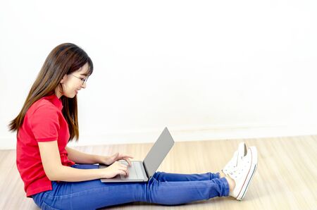 A beautiful Asian woman wearing a red shirt, eyeglasses, smiling with a notebook computer.の写真素材