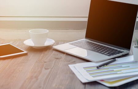 A notebook computer on the table.Brown table top There is equipment to work on it.A white coffee cup...