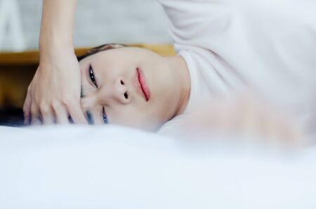 Asian women are headache severely.Lady wake up in the morning with migraine.Insomnia results in headaches when awakened.Young girl sitting on a stressed bed.の写真素材