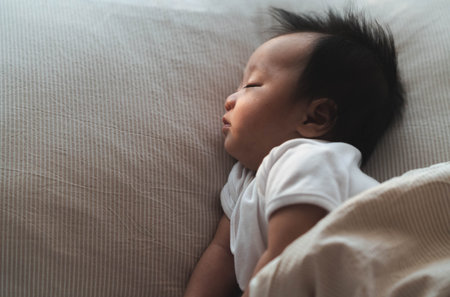 A serene image of a baby sleeping soundly on a pillow, wrapped in a soft blanket. The gentle morning light highlights the baby's calm expression, capturing a quiet and peaceful moment of rest.の写真素材