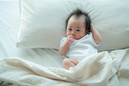 A peaceful image of a baby lying on a soft bed, gently resting against a pillow with morning light streaming through the window. The baby's calm expression and cozy surroundings create a warm and comforting atmosphere, capturing the essence of early childhood and family moments.の写真素材
