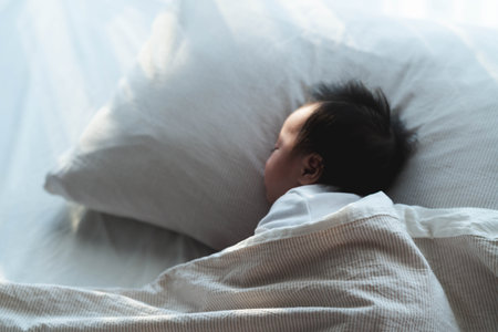 A serene image of a baby sleeping soundly on a pillow, wrapped in a soft blanket. The gentle morning light highlights the baby's calm expression, capturing a quiet and peaceful moment of rest.の写真素材