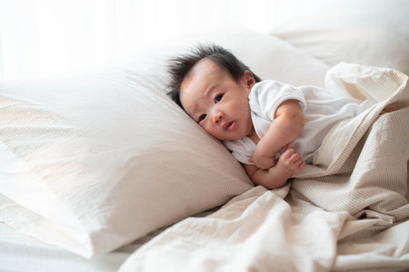 A peaceful image of a baby lying on a soft bed, gently resting against a pillow with morning light streaming through the window. The baby's calm expression and cozy surroundings create a warm and comforting atmosphere, capturing the essence of early childhood and family moments.の写真素材