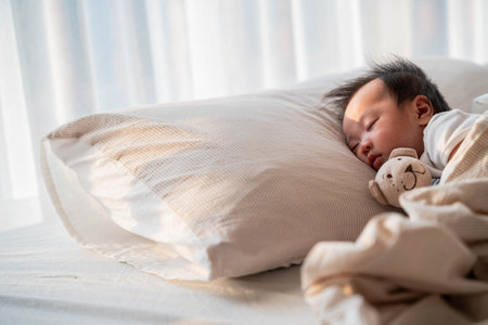 A serene image of a baby sleeping soundly on a pillow, wrapped in a soft blanket. The gentle morning light highlights the baby's calm expression, capturing a quiet and peaceful moment of rest.の写真素材