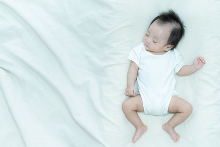 A serene image of a baby sleeping peacefully on a soft white blanket. The baby's relaxed posture and calm expression capture the tranquility and innocence of early childhood.の写真素材