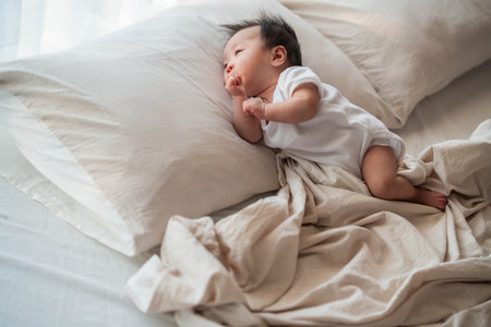 A serene image of a baby sleeping soundly on a pillow, wrapped in a soft blanket. The gentle morning light highlights the baby's calm expression, capturing a quiet and peaceful moment of rest.の写真素材