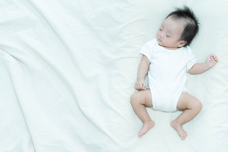 A serene image of a baby sleeping peacefully on a soft white blanket. The baby's relaxed posture and calm expression capture the tranquility and innocence of early childhood.の写真素材