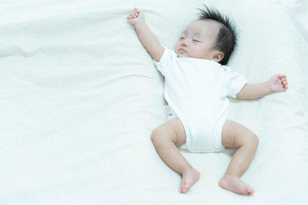 A serene image of a baby sleeping peacefully on a soft white blanket. The baby's relaxed posture and calm expression capture the tranquility and innocence of early childhood.の写真素材