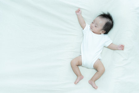 A serene image of a baby sleeping peacefully on a soft white blanket. The baby's relaxed posture and calm expression capture the tranquility and innocence of early childhood.の写真素材