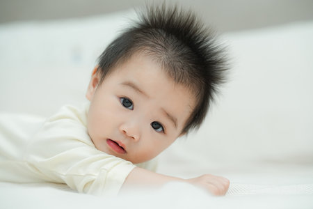 A close-up shot of a baby lying on their tummy on a soft, textured cushion. The baby's wide-eyed and curious expression captures a precious moment of early development as they engage with their surroundings.の写真素材