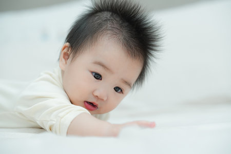 A close-up shot of a baby lying on their tummy on a soft, textured cushion. The baby's wide-eyed and curious expression captures a precious moment of early development as they engage with their surroundings.の写真素材