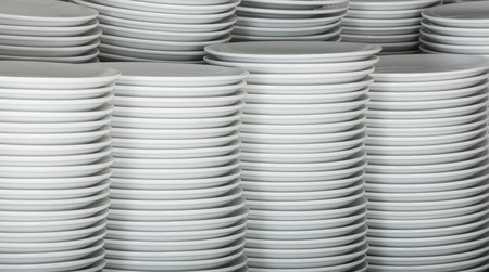 Stacks of many white plates on a wire rack shelf in a commercial kitchenの写真素材
