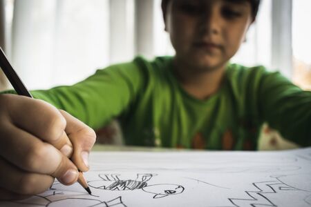 Close up of child's hands drawing at white paper within colorful pens and pencils.の写真素材