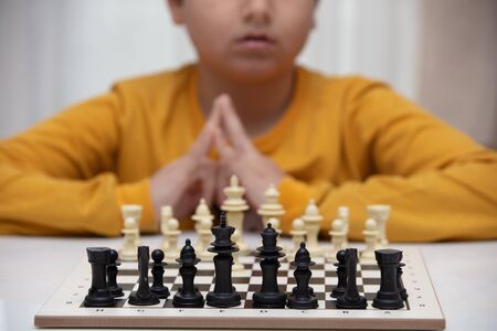 sits at a table and plays chess. The kid concentrated on the game