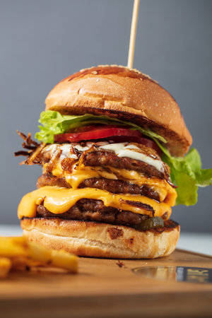 Loaded cheeseburgers three triple, stacked patties stacked high with layers of cheese, lettuce, and tomato. Tall cheeseburger. High quality photoの写真素材