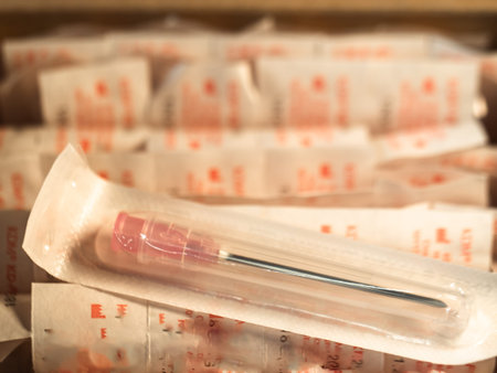 Sterile medical needles in clear packaging sit in rows. Each needle sealed with protective plastic...