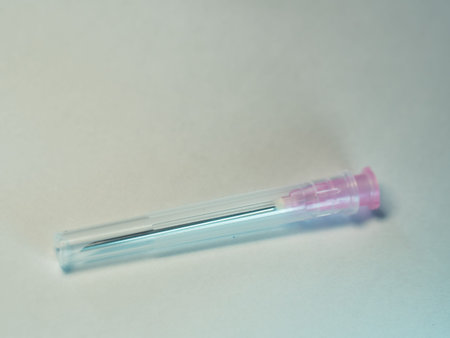 Clear plastic tube holds sharp medical needle. Pink cap seals the tip for safety. Simple background...