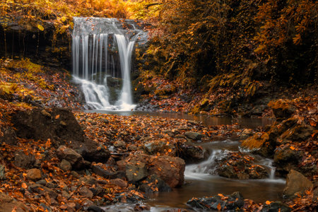 Beautiful waterfall in the autumn forest with fallen leaves on the rocksの写真素材