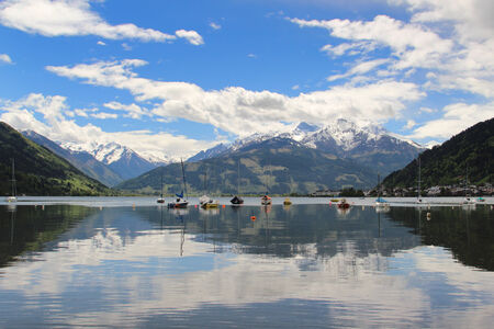 Anchored boats on the lake of Zell am See with beautiful summer alpine mountains in the backgroundの写真素材