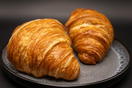 Two croissants on a black plate on a dark background.の写真素材