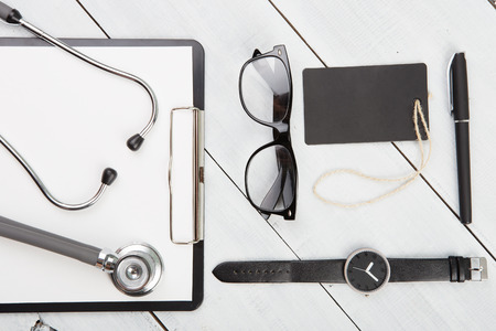 Workplace of doctor - stethoscope, medicine clipboard, glasses and watches on wooden deskの写真素材