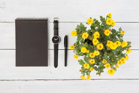 Notepad, watches, pen and flower vase on a wooden table