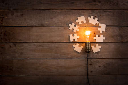 Idea and teamwork business concept - vintage incandescent light bulb and jigsaw on the wooden backgroundの写真素材