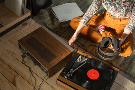 Young Woman listening to a music on a HiFi system with turntable, amplifier, headphones and lp vinyl records in a listening roomの写真素材