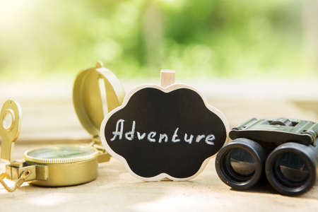 Plan your adventure concept - Adventure written on a small sign, compass and binocular outdoors, green blurred backgroundの写真素材