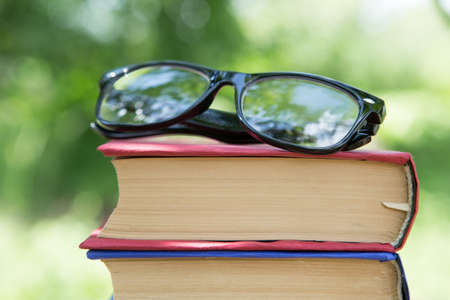 Books and eyeglasses on a wooden table in a garden. Sunny summer day reading in a vacation conceptの写真素材