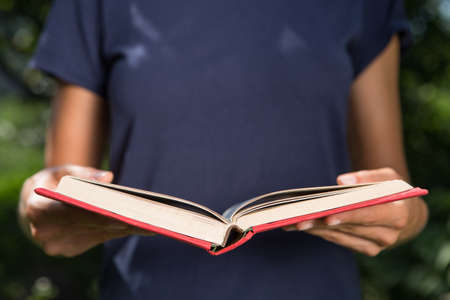 Reading and education in summer concept, girl holding an open book, reading outdoors in a gardenの写真素材