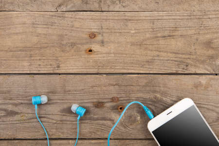 White smartphone with headphones on the old wooden boardの写真素材