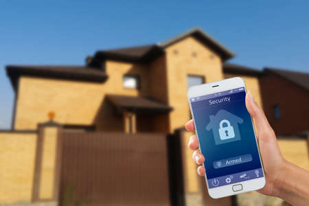 Smartphone with home security app in a hand on the building backgroundの写真素材