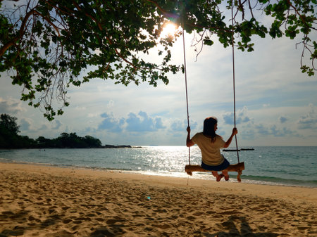 A girl sitting on swing on a sandy beach vacation freedomの写真素材
