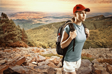 Young woman climber wearing cap with backpack hiking in mountain and hills  Satisfied female traveler in sportswear trekking on sunset の写真素材