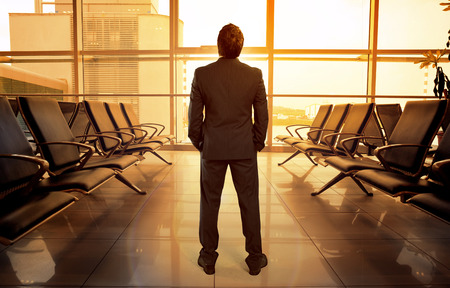 Business man standing in airport hall waiting his flight. Beautiful view of lonely male passenger looking through glass window in airport terminal.の写真素材